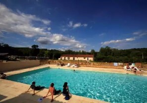 A swimming pool with clear blue water, surrounded by a wooden fence and a few people relaxing.