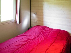 A room with a bed, a window with curtains, and a wooden wall. - ZEcamping 3 étoiles piscine chauffée dog friendly cottage TV LV clim 35m2 (Cazals)