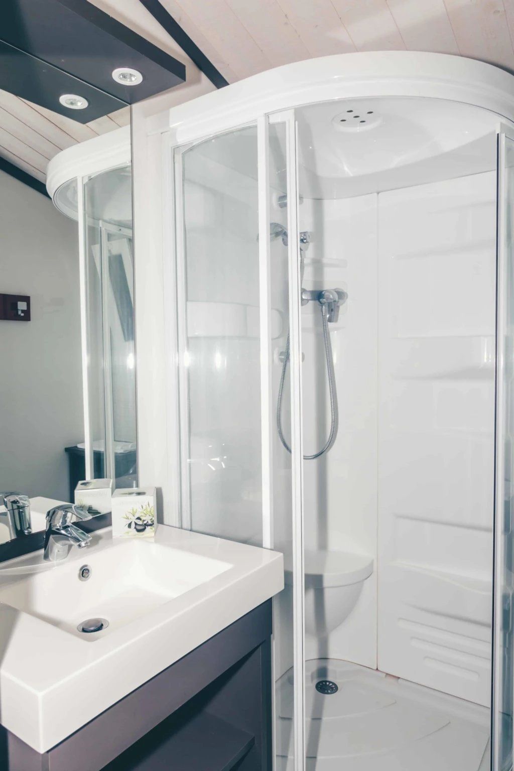 A modern bathroom with a white sink, a glass-enclosed shower, and a large mirror.