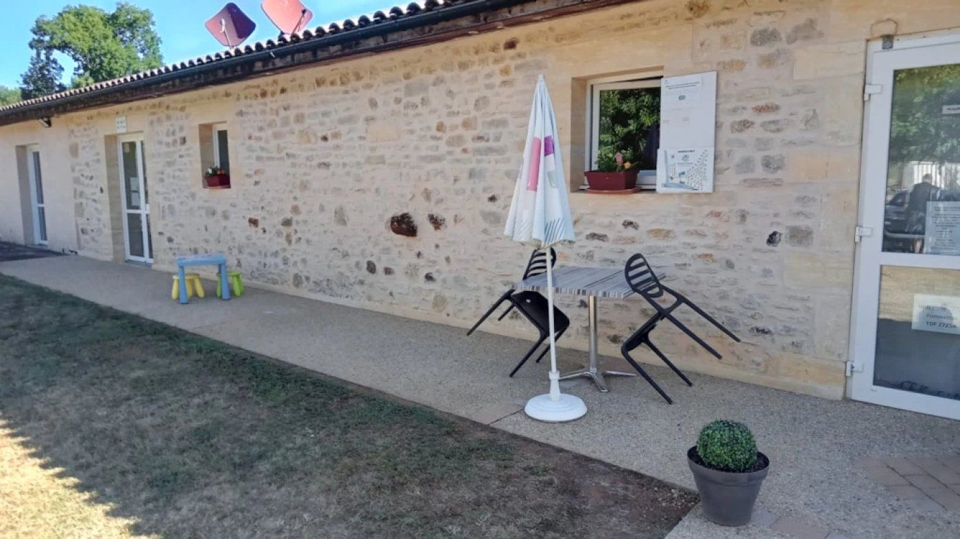A stone building with a door, a window, and a small table with chairs outside.