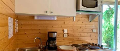 A compact kitchen with wooden walls, a microwave, a coffee maker, and a sink.