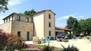 Un edificio de dos pisos con fachada de piedra y techo de tejas. Hay áreas de estar al aire libre con sillas y mesas.