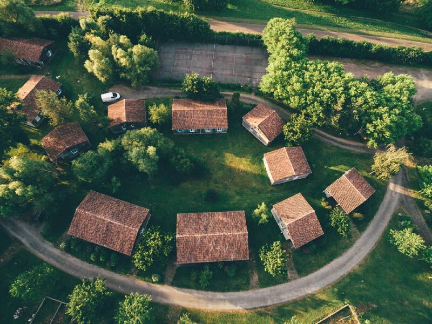 Eine Vogelperspektive auf eine Gruppe traditioneller Häuser mit geneigten Dächern, umgeben von üppigem Grün und einer gewundenen Straße.