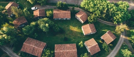 Une vue aérienne d’un ensemble de maisons traditionnelles aux toits inclinés, entourées d’une végétation luxuriante et bordées d’une route sinueuse.