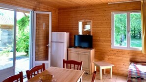 Une cabane en bois comprenant une table à manger, des chaises, un téléviseur et un réfrigérateur.