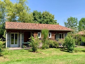 A two-story wooden house with a tiled roof, a covered porch, and a small lawn. - ZEcamping 3 étoiles animaux acceptés piscine snack bar et restaurant (Moutiers-sous-Chantemerle)