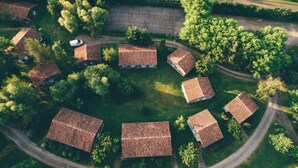 An aerial view of a cluster of traditional houses with sloped roofs, surrounded by lush greenery and a winding road.
