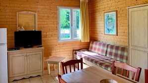 A wooden cabin with a television on a cabinet, a sofa, a table, and two windows with curtains.