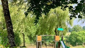 A playground with a slide and climbing structures, surrounded by trees and grass.