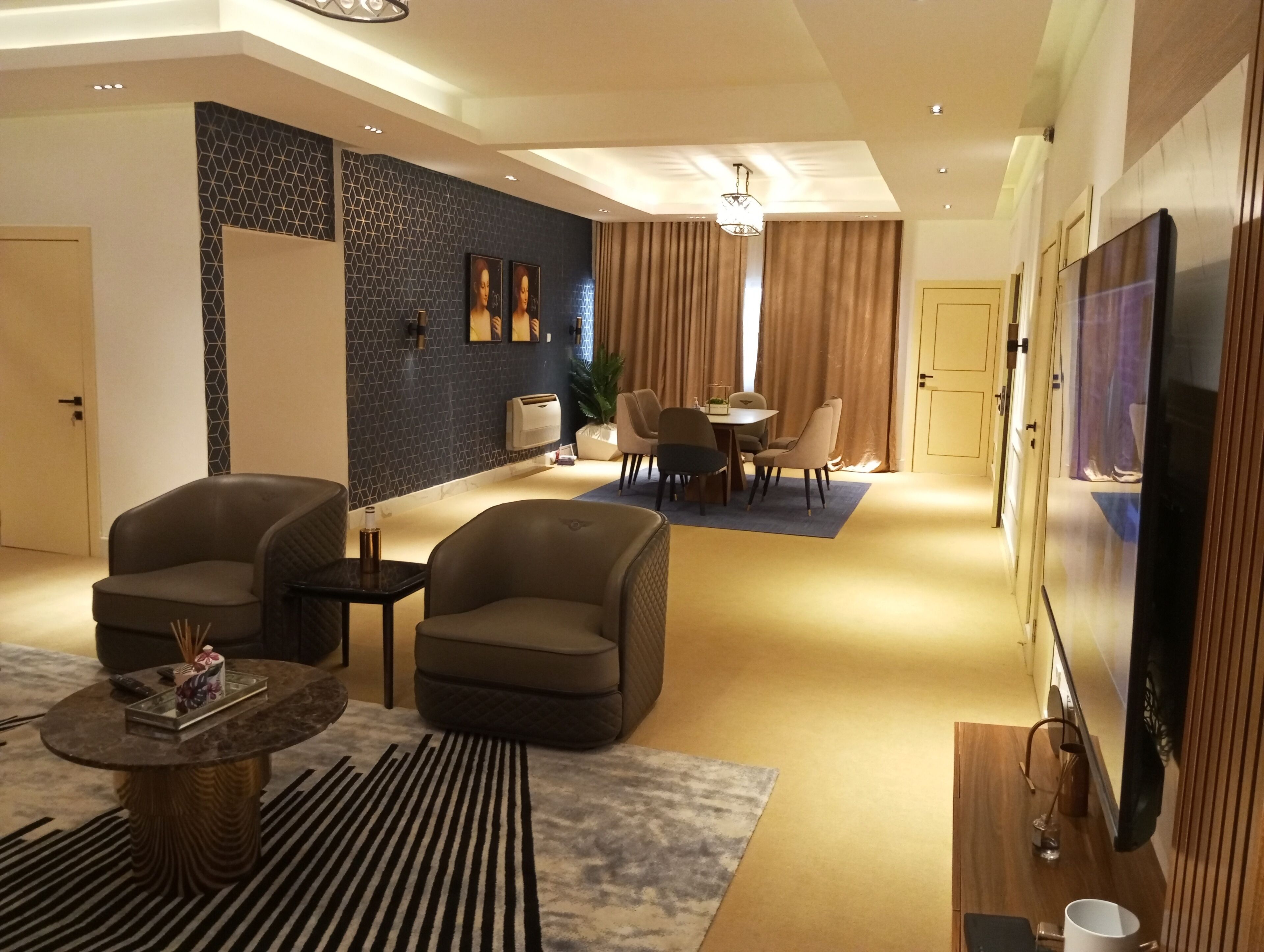 Un salon moderne avec un canapé, des fauteuils, une table basse et un téléviseur. On aperçoit à l’arrière-plan un coin repas avec une table et des chaises.