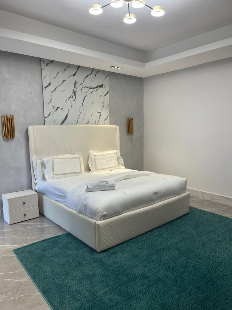 Ein modernes Schlafzimmer mit einem großen Bett, einem Nachttisch, einer Marmorwand und einer Deckenleuchte.