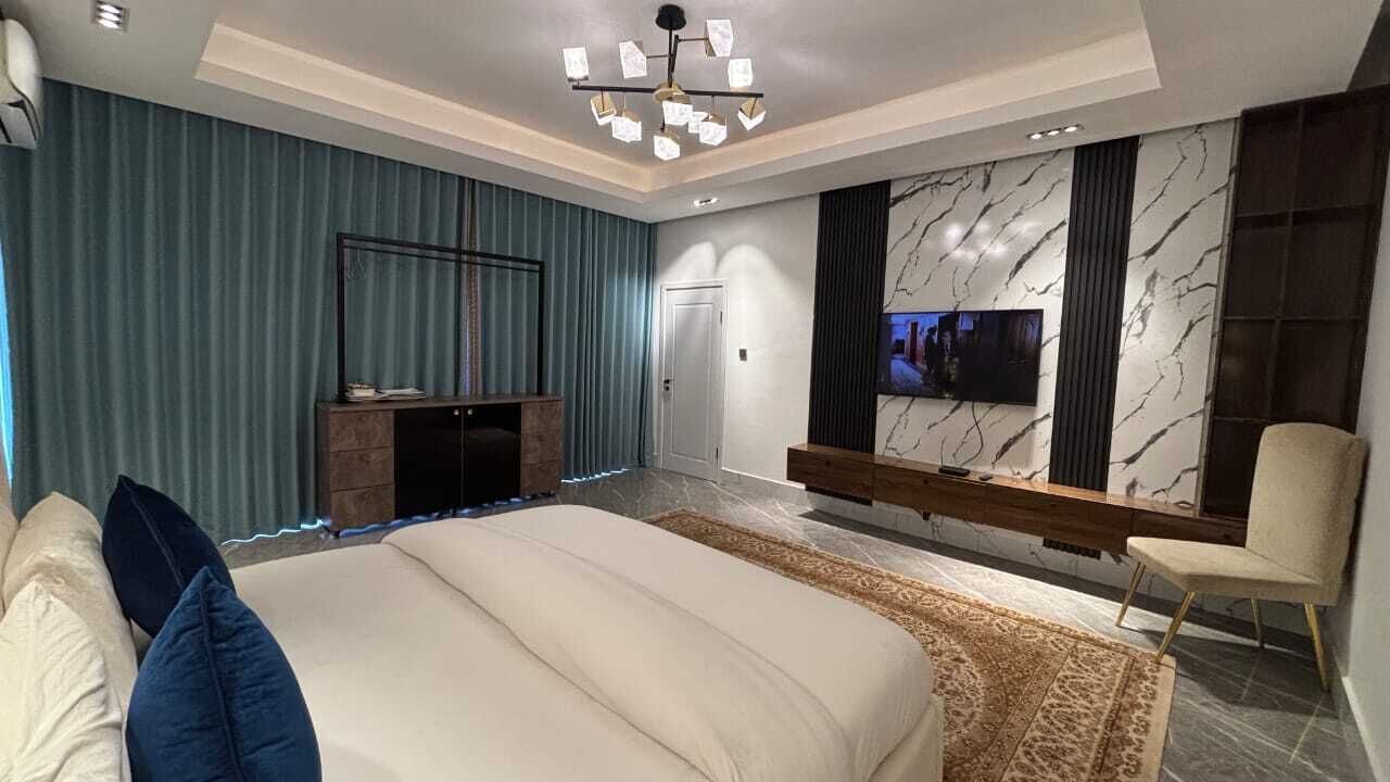 Une chambre à coucher moderne avec un grand lit, un téléviseur fixé au mur et une cheminée.