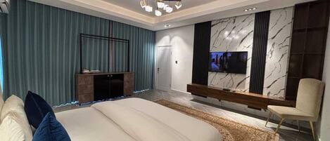 Une chambre à coucher moderne avec un grand lit, un téléviseur fixé au mur et une cheminée.