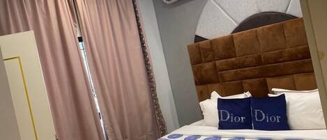 A hotel room with a large bed, a headboard, a ceiling light, an air conditioning unit, and a patterned floor.
