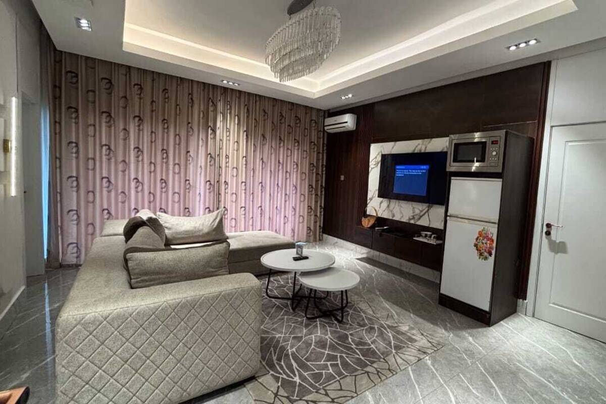 A modern living room with a sofa, two round tables, a TV, and a built-in kitchen area with a microwave and oven.