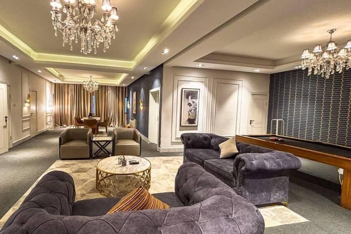 A spacious living room with a pool table, comfortable seating, and a chandelier.