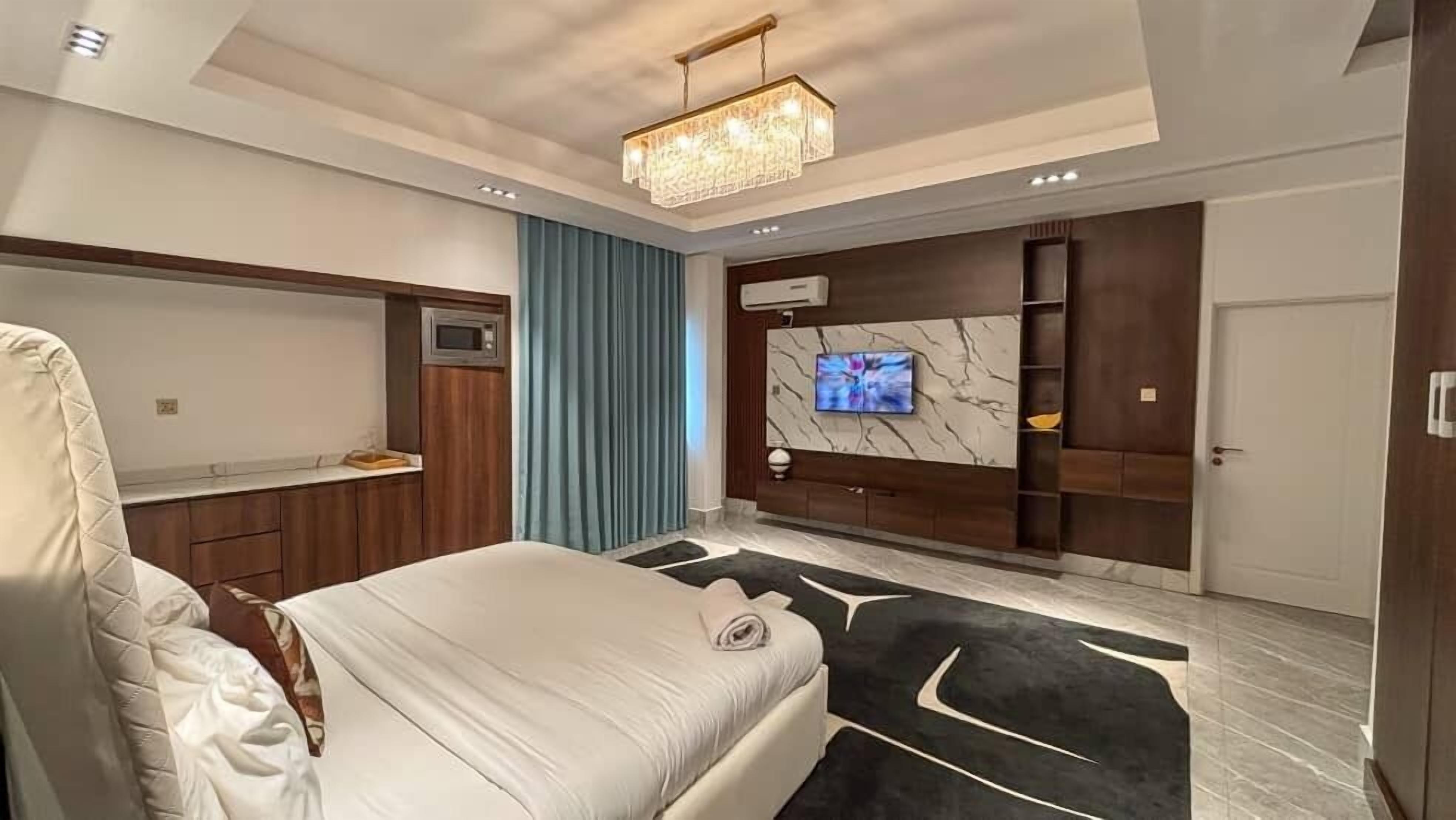 Un dormitorio moderno con una cama grande, televisión instalada en una pared de mármol y un armario empotrado.