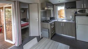 A compact kitchen with a gas stove, microwave, and refrigerator, a small dining table, and a sliding door leading to an outdoor area. - ZEcamping 4 étoiles animé chiens acceptés familial piscine couverte (Saint-Michel-Escalus)