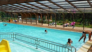 An indoor swimming pool with a glass ceiling and a poolside area with lounge chairs and umbrellas. - ZEcamping 4 étoiles animé chiens acceptés familial piscine couverte (Saint-Michel-Escalus)