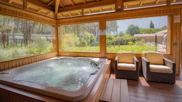 A wooden spa area with a hot tub, two wicker chairs, and large windows offering a view of the outdoors. - ZEcamping 4 étoiles animé chiens acceptés familial piscine couverte (Saint-Michel-Escalus)