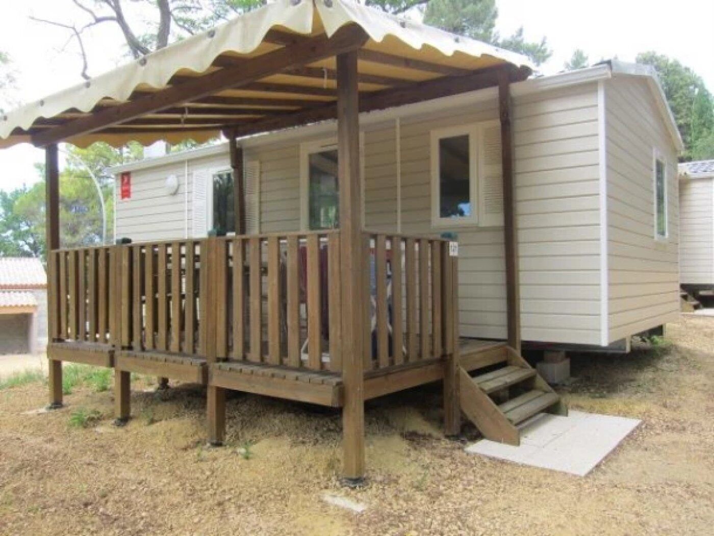Ein kleines, eingeschossiges Mobilheim mit einer Holzterrasse und einer überdachten Veranda.