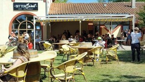 Ein Außenbereich mit Tischen und Stühlen, ein überdachter Bereich und ein Gebäude mit der Aufschrift 'BitterSweet Cafe - Restaurant'.