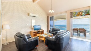 A modern living room with a large window overlooking a scenic view, a flat-screen TV, and a cozy seating area. - Classic View 2, 2 49 Victoria Pde - panoramic water views, aircon, free Wifi (Nelson Bay)