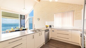 A modern kitchen with a view of the sea, a dining area with a table set for two, and a large window with blinds. - Classic View 2, 2 49 Victoria Pde - panoramic water views, aircon, free Wifi (Nelson Bay)