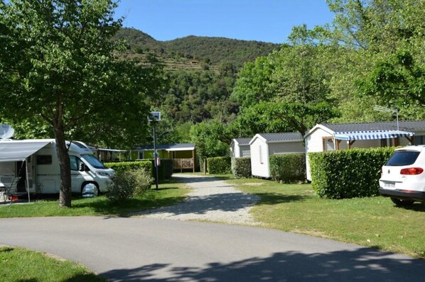 Un terrain de camping avec des camping-cars et des mobil-homes, un chemin de gravier et une montagne en arrière-plan.