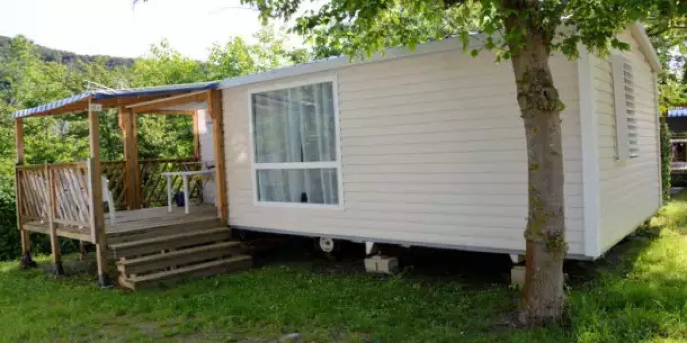 Una casa móvil con porche y escalones, rodeada de vegetación.