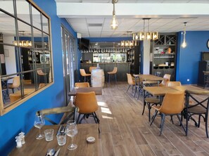 A restaurant interior with wooden tables and chairs, a bar area, and a large window. - ZEcamping 3 étoiles familial piscine chauffée mobil-home TV clim 28m2 (Amélie-les-Bains-Palalda)