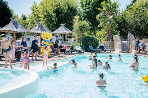 Ein Poolbereich mit Menschen, die das Wasser genießen, umgeben von Palmen und beschattet durch Strohdachschirme.