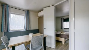 A compact room with a dining table and chairs, a bed, and a window with curtains.