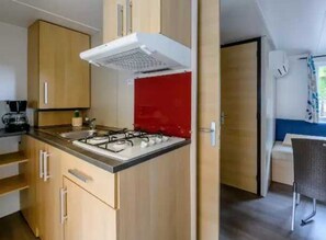 A compact kitchen with a gas stove, a coffee maker, and a red backsplash.