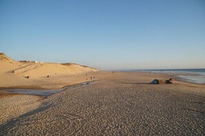 Una amplia playa arenosa con dunas suaves y cielo despejado.