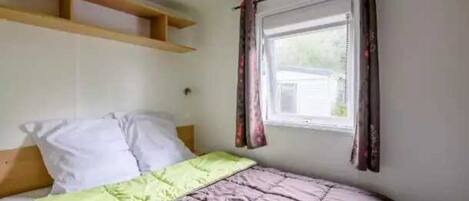 Una cama individual con un edredón verde y marrón, un cabecero de madera y una ventana con cortinas.