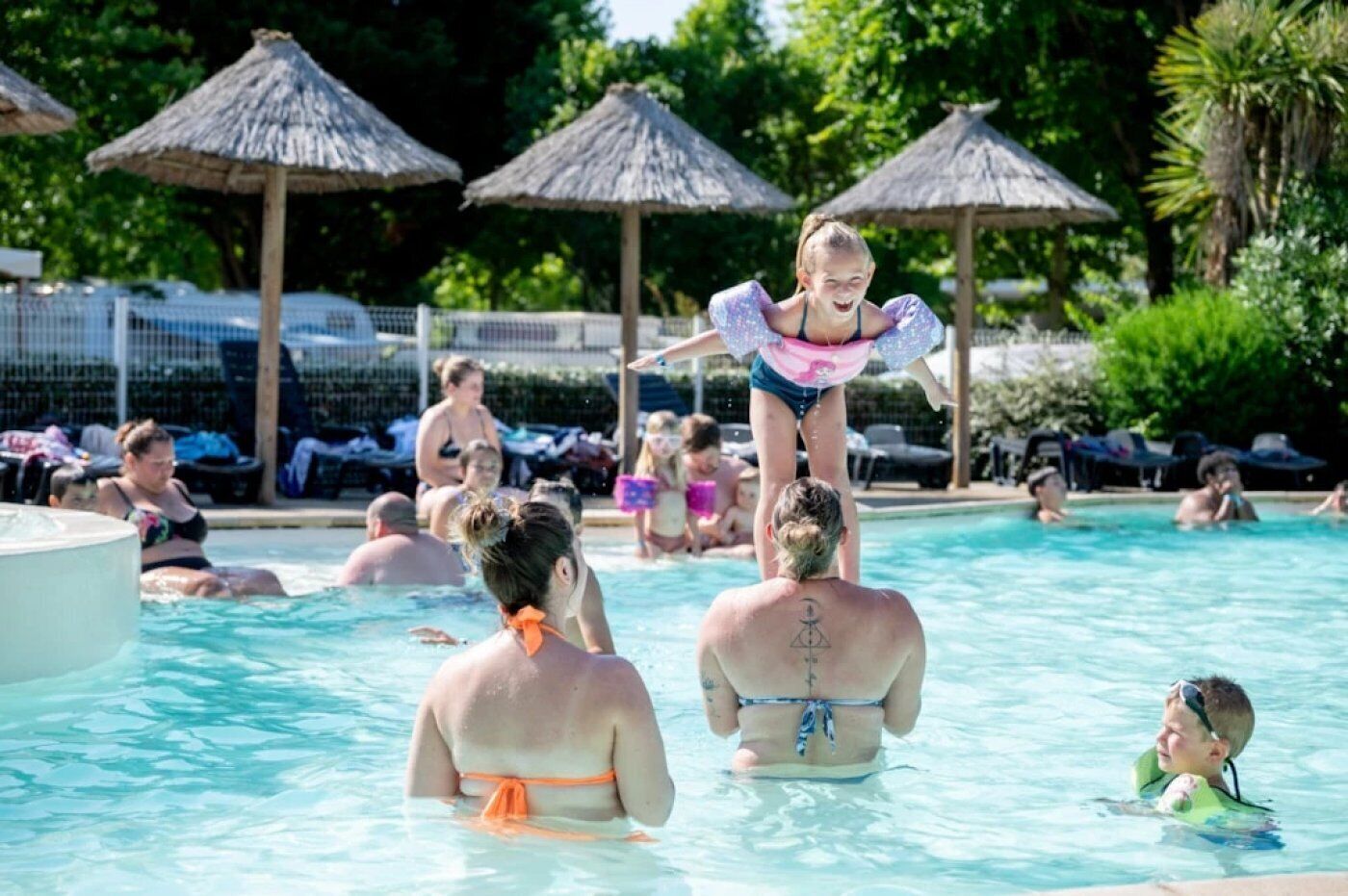 A swimming pool with people enjoying the water, surrounded by umbrellas and lounge chairs.