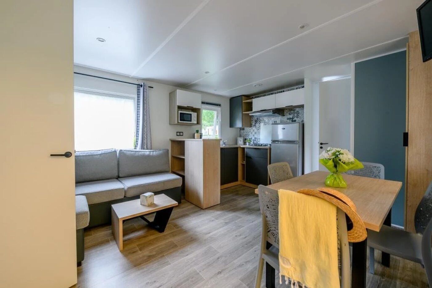 Een knus woongedeelte met een kitchenette, een bank, een eettafel en een klein bijzettafeltje.
