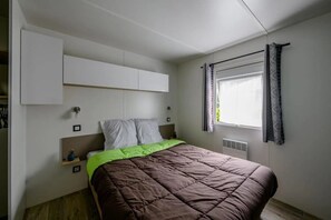 Un dormitorio con cama, armarios blancos, una ventana con cortinas y un radiador.