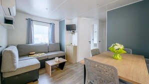 Un espacio habitable moderno y funcional con sofá, una mesita, una mesa de comedor con sillas, un televisor en la pared y una ventana con cortinas.