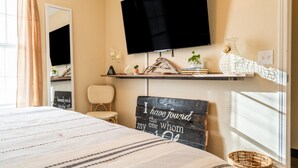 A bedroom with a bed, a flat-screen TV mounted on the wall, a bedside table with a lamp, a chair, and a decorative sign. - Townhome with a peaceful, soothing vibe, featuring KING and QUEEN size beds (Springdale)