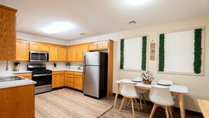 A modern kitchen with wooden cabinets, stainless steel appliances, a dining area with a table and chairs, and decorative greenery on the windows. - Townhome with a peaceful, soothing vibe, featuring KING and QUEEN size beds (Springdale)