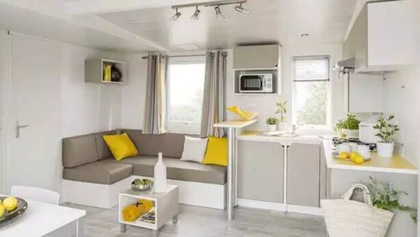 Ein moderner, kompakter Wohnraum mit Sofa, einem kleinen Tisch, einer Küchenzeile mit Mikrowelle und einem Esstisch.