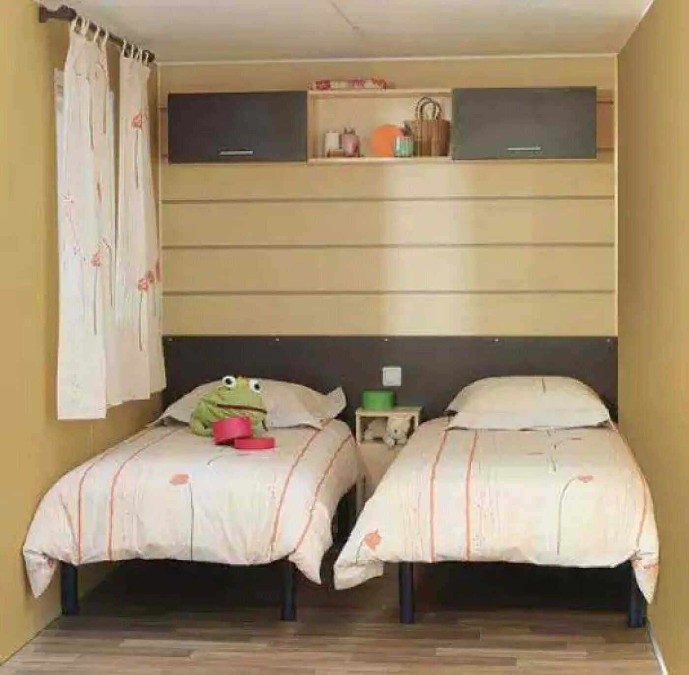 Une chambre avec deux lits, une petite étagère où sont posés des objets personnels et un rideau.