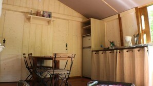 En inredning med träpanel, ett matbord och stolar, ett köksområde med ett kylskåp och ett fönster med gardiner.