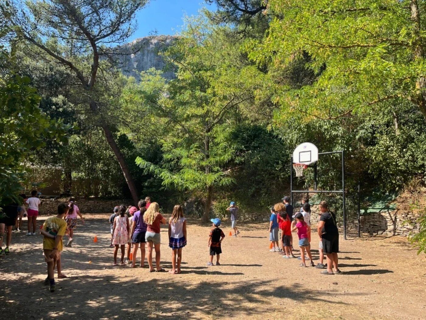 An outdoor basketball court surrounded by trees and a stone wall.