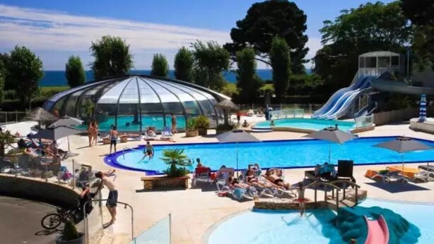 A pool area with a large central pool, a smaller pool, and a water slide. - ZEcamping 4 étoiles 200m plage piscine couverte locatif TV LV BBQ 32m2 (Névez)