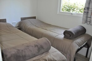 Een eenvoudige kamer met twee bedden, een raam met gordijnen en een klein tafeltje.