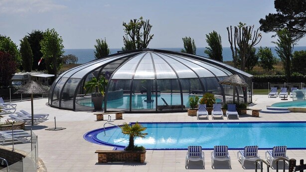Un espace piscine entièrement vitré, avec des chaises longues et une vue sur la mer.