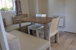 Een kamer met een houten eettafel, witte stoelen, een bank en een raam met gordijnen.